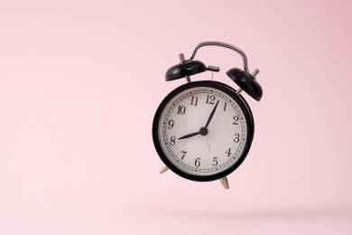 粉色背景前，跳跃的黑色闹钟