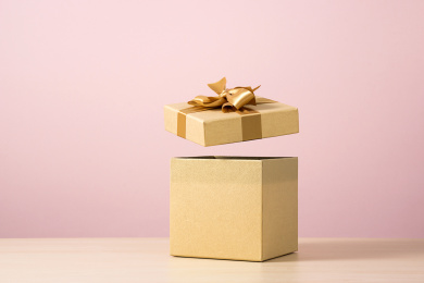粉色背景前，打开盖子的金色礼物盒