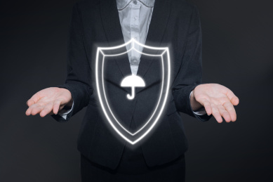 黑色背景下穿着西装正装的人双手之间有一个护盾保护伞象征着平安和保护保险
