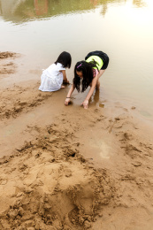 在水边开心玩泥沙的小女孩