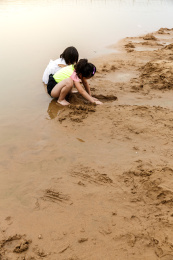 在水边开心玩泥沙的小女孩