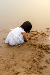 在水边开心玩泥沙的小女孩