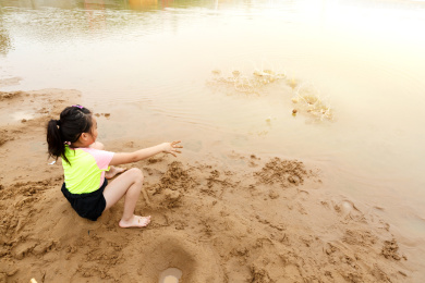 在水边开心玩泥沙的小女孩