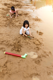 在水边开心玩泥沙的小女孩