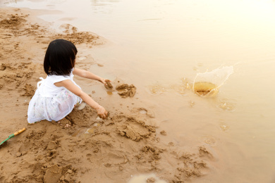 在水边开心玩泥沙的小女孩