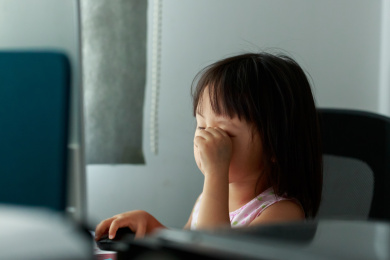 坐在电脑前玩电脑游戏的小女孩揉眼睛