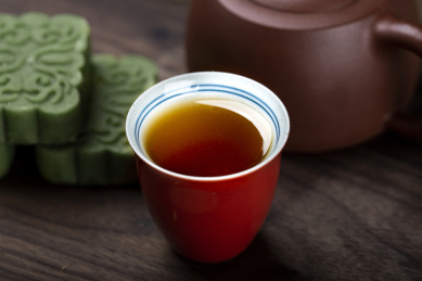 珊瑚红小杯里面盛满了祁眉红茶茶汤，搭配绿色龙井茶糕，朱红色紫砂小壶