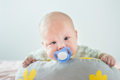 白色背景前趴在软垫上的初生婴儿和安抚奶嘴