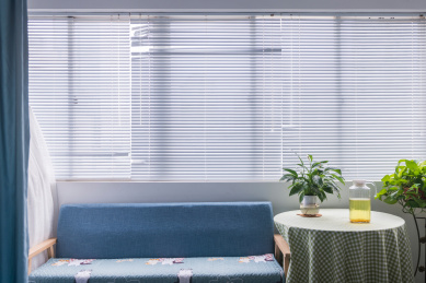 百叶窗前的沙发和摆放有白掌绿植和荞麦茶的茶几