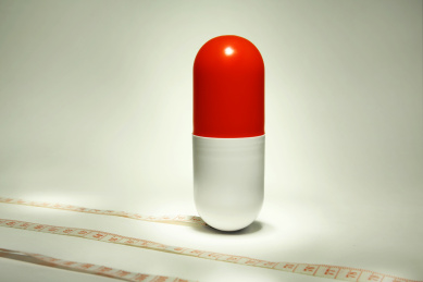 一颗胶囊和卷尺放在灰色背景上，象征着药物减肥塑身。