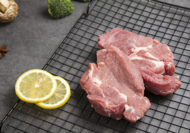 两块放在台面上的新鲜梅头瘦肉和烧烤网柠檬片