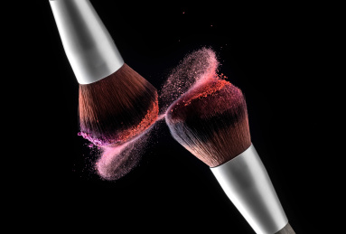 沾满粉底的化妆刷在黑色背景下相碰一瞬间