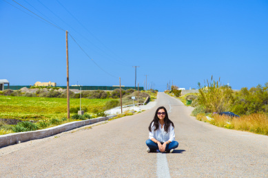 亚裔女性性在希腊圣托里尼岛的马路中间坐着微笑看向镜头