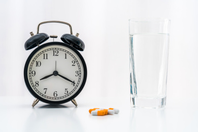 白色桌面上的胶囊、闹钟和一杯水