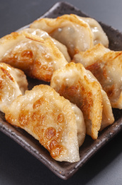 被油煎的金黄色的煎饺盛放在深色碟子中与中国结摆放在桌面上