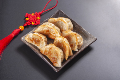 被油煎的金黄色的煎饺盛放在深色碟子中与中国结摆放在桌面上