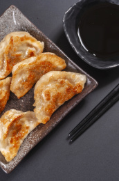 被油煎的金黄色的煎饺盛放在深色碟子中与中国结摆放在桌面上