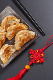 被油煎的金黄色的煎饺盛放在深色碟子中与中国结摆放在桌面上