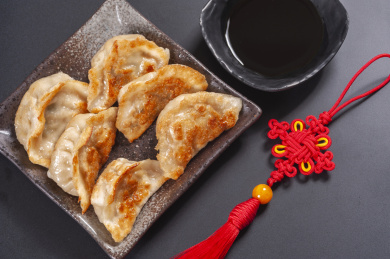 被油煎的金黄色的煎饺盛放在深色碟子中与中国结摆放在桌面上