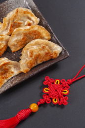 被油煎的金黄色的煎饺盛放在深色碟子中与中国结摆放在桌面上