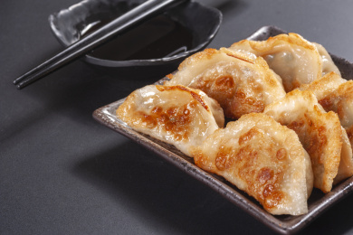 被油煎的金黄色的煎饺盛放在深色碟子中与中国结摆放在桌面上