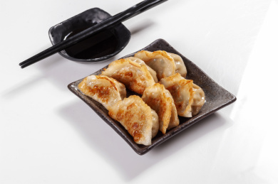 被油煎的金黄色的煎饺盛放在深色碟子中与中国结摆放在桌面上