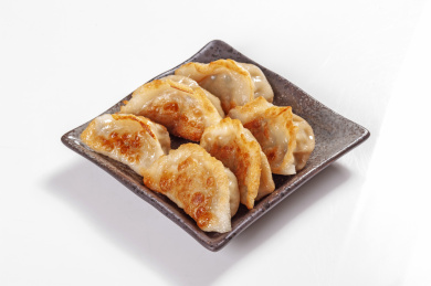 被油煎的金黄色的煎饺盛放在深色碟子中与中国结摆放在桌面上