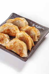 被油煎的金黄色的煎饺盛放在深色碟子中与中国结摆放在桌面上