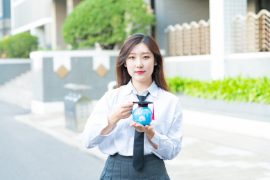 一个青春清纯美女大学生在校园内手拿着毕业服毕业帽地球仪开心的微笑