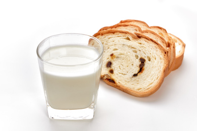 白色背景前放着一玻璃杯牛奶和切片面包的素食早餐