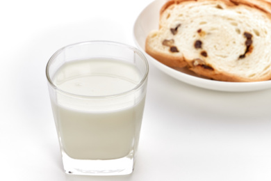 白色背景前放着一玻璃杯牛奶和切片面包的素食早餐