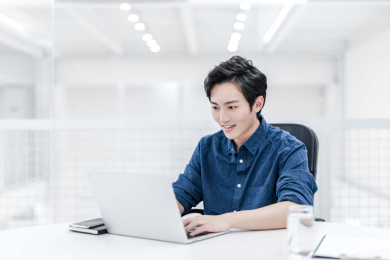 一位亚洲男性白领坐在办公桌前使用笔记本电脑