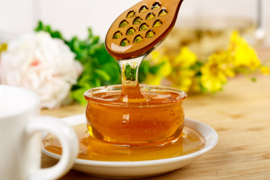 桌面上从蜂蜜搅拌棒向杯子里滴落的蜂蜜