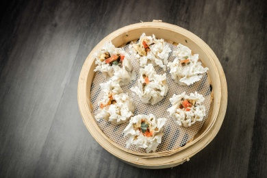 暗色木纹桌上放着一笼三鲜馅烧麦