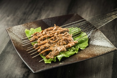 暗色木纹桌面上放着一盘烤熟的鲜肉串