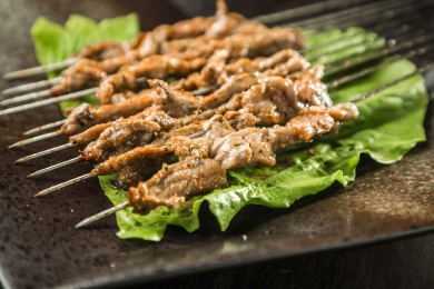 暗色木纹桌面上放着一盘烤熟的鲜肉串