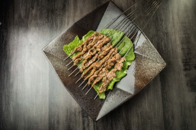 暗色木纹桌面上放着一盘烤熟的鲜肉串