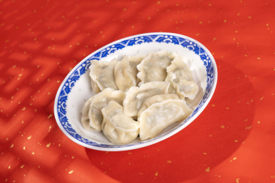 传统美食水饺盛放在青花碟子中摆放在喜庆的洒金红色背景上