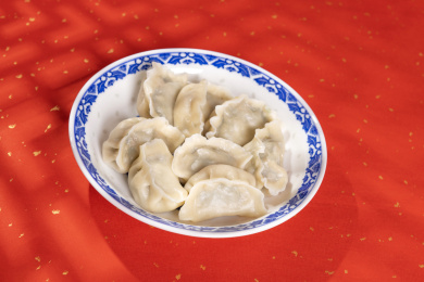传统美食水饺盛放在青花碟子中摆放在喜庆的洒金红色背景上