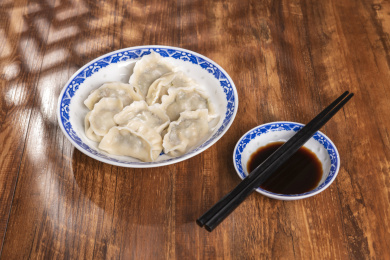 传统美食水饺盛放在青花碟子中摆放在窗影下的木桌上旁边放有中国结
