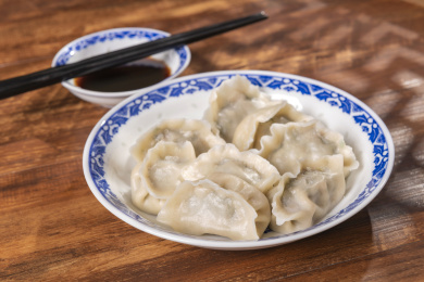 传统美食水饺盛放在青花碟子中摆放在窗影下的木桌上旁边放有中国结