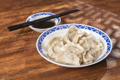 传统美食水饺盛放在青花碟子中摆放在窗影下的木桌上旁边放有中国结