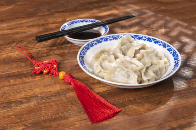 传统美食水饺盛放在青花碟子中摆放在窗影下的木桌上旁边放有中国结