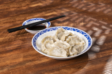 传统美食水饺盛放在青花碟子中摆放在窗影下的木桌上旁边放有中国结