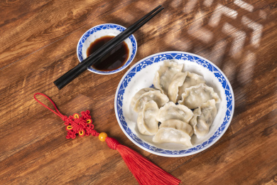 传统美食水饺盛放在青花碟子中摆放在窗影下的木桌上旁边放有中国结