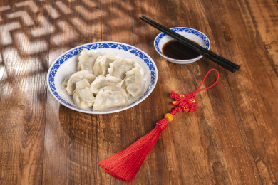 传统美食水饺盛放在青花碟子中摆放在窗影下的木桌上旁边放有中国结