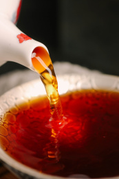 茶壶中倒出褐色普洱熟茶茶汤到银纸的茶杯中