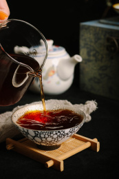 黑色背景上的褐色普洱茶汤倒在银制的杯子中