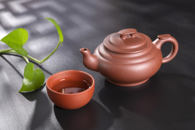 窗影下的黑色桌面上摆放着传统茶具紫砂壶及紫砂杯