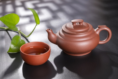 窗影下的黑色桌面上摆放着传统茶具紫砂壶及紫砂杯